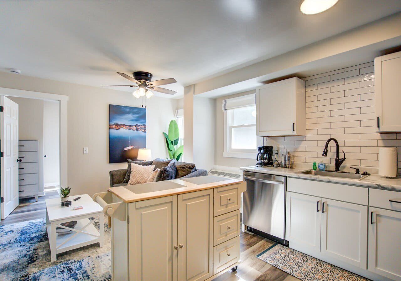 Open-concept kitchen and living area with stainless steel appliances, movable island, and cozy seating. Large windows bring in natural light, creating a bright, welcoming space for dining and relaxation.