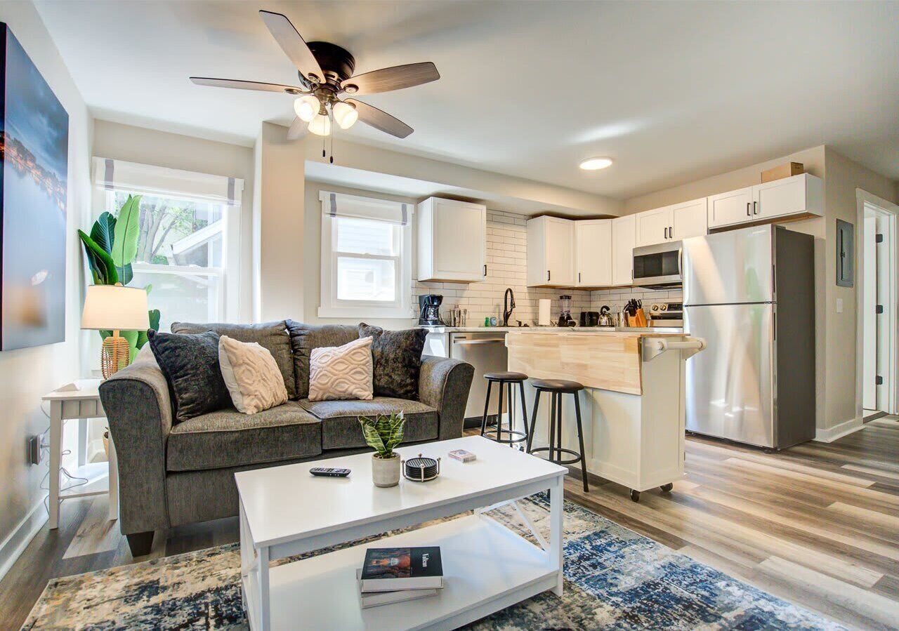 right open living area with a plush sofa, modern décor, and plenty of natural light. The space flows into the updated kitchen with stainless steel appliances and a breakfast bar, perfect for relaxing or entertaining.