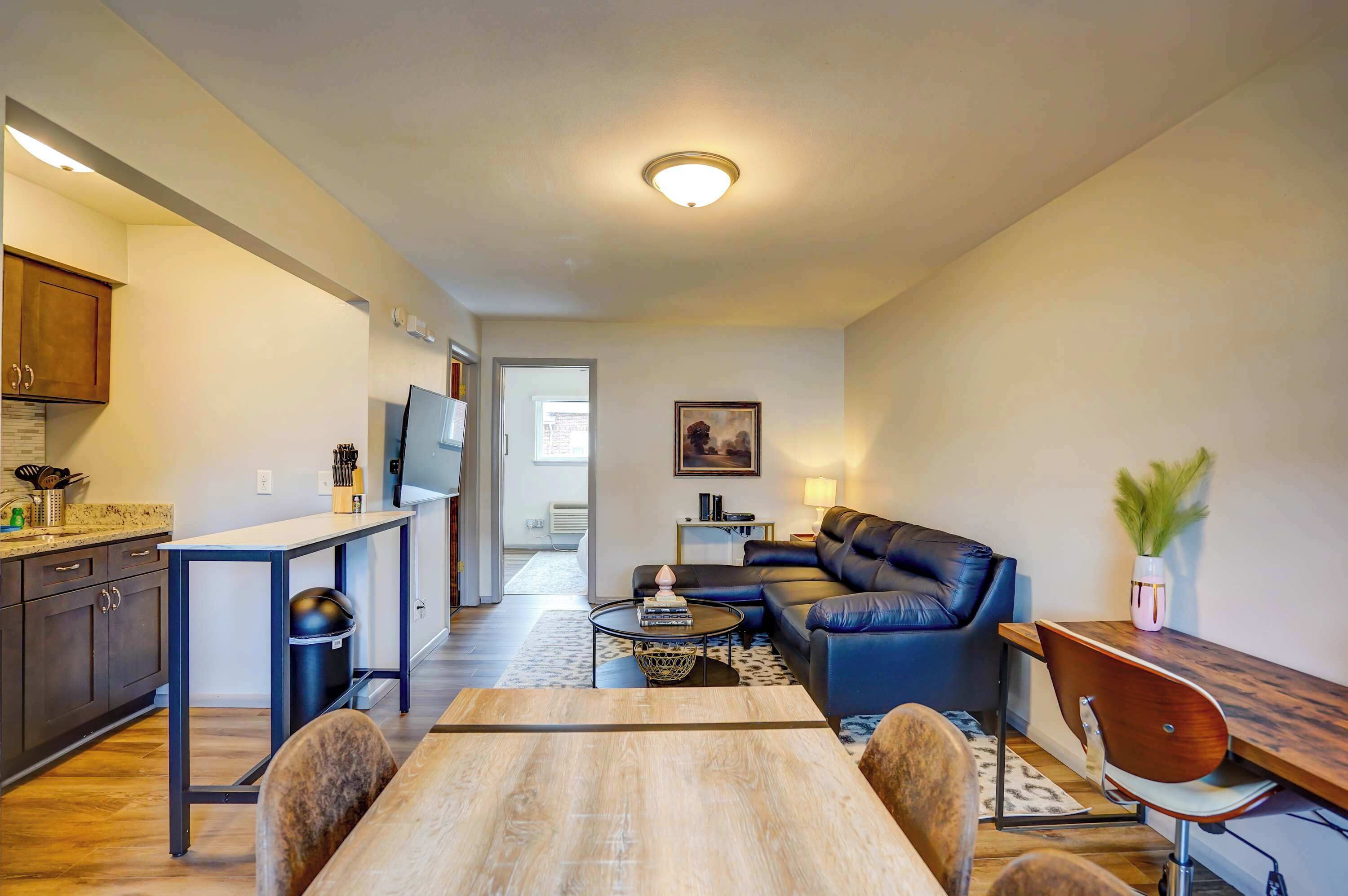 Eine moderne Wohnung mit Essbereich, Wohnzimmer mit Sofa, Küche mit dunklen Schränken und einem Flur, der in einen weiteren Raum führt.