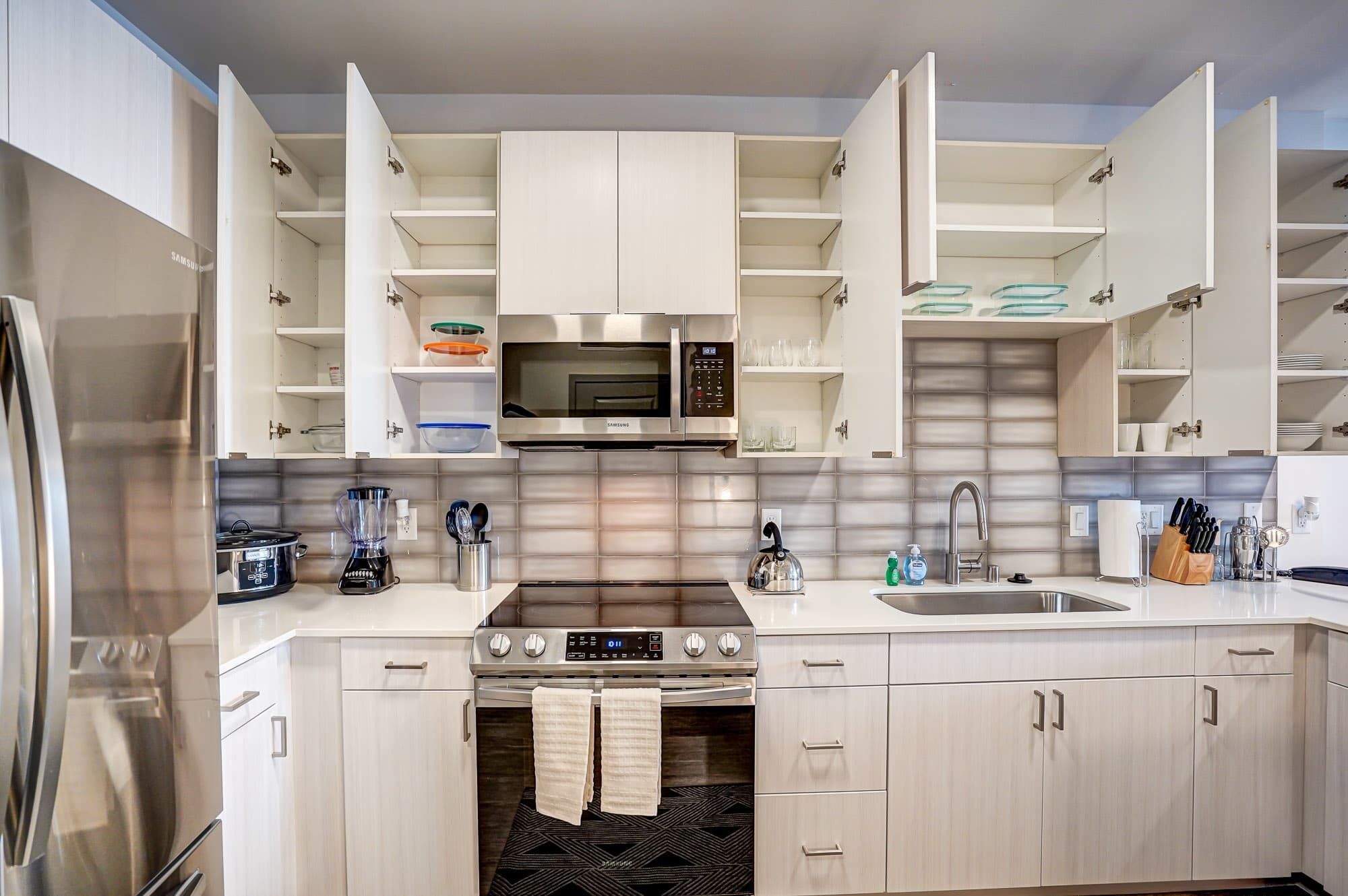 Kitchen with stainless appliances, modern backsplash, and open cabinets revealing glassware and dishes, fully stocked for cooking or dining in.