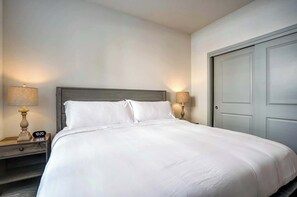 Serene bedroom with a plush queen bed, soft white linens, and matching nightstands with warm lamps. Sliding-door closet offers ample storage, creating a calm retreat for restful nights. - Modern Apt with Pool, Parking & Pet Wash (Madison)