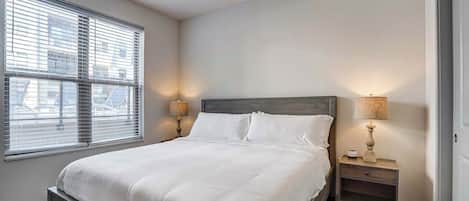 Inviting bedroom with a queen-size bed dressed in crisp white linens, dual nightstands with warm lamps, and a large window for plenty of natural light.