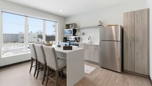 Une cuisine moderne dotée d’un îlot central, d’appareils électroménagers en acier inoxydable et offrant une vue sur l’extérieur.