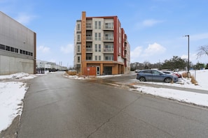 A multi-story building with a red and beige facade, a visible entrance, and a parking lot with cars. - Near MCW | Free Parking & In-Unit Laundry (Milwaukee)