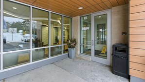 Une entrée d’immeuble avec une façade en verre, un plafond en bois et une enseigne indiquant l’adresse « 9150 ».
