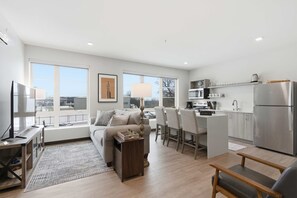 A modern apartment with a living room, dining area, and kitchen. There are large windows, a flat-screen TV, and a dining table with chairs. - Near MCW | Free Parking & In-Unit Laundry (Milwaukee)