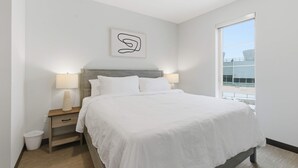 Une chambre moderne avec un grand lit, deux lampes de chevet, une table de chevet, une petite poubelle et une œuvre d’art abstraite accrochée au mur.