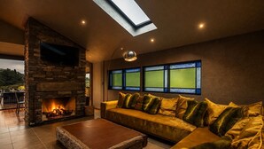 Ein gemütliches Wohnzimmer mit Kamin aus Stein, einer Couch mit Kissen, einem Couchtisch und einem Oberlicht.