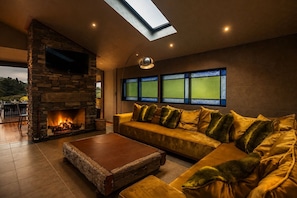 A cozy living room with a stone fireplace, a sofa with cushions, a coffee table, and a skylight. - Maison Blanc Lodge - Nature Haven 4-Bed Luxury (Auckland)