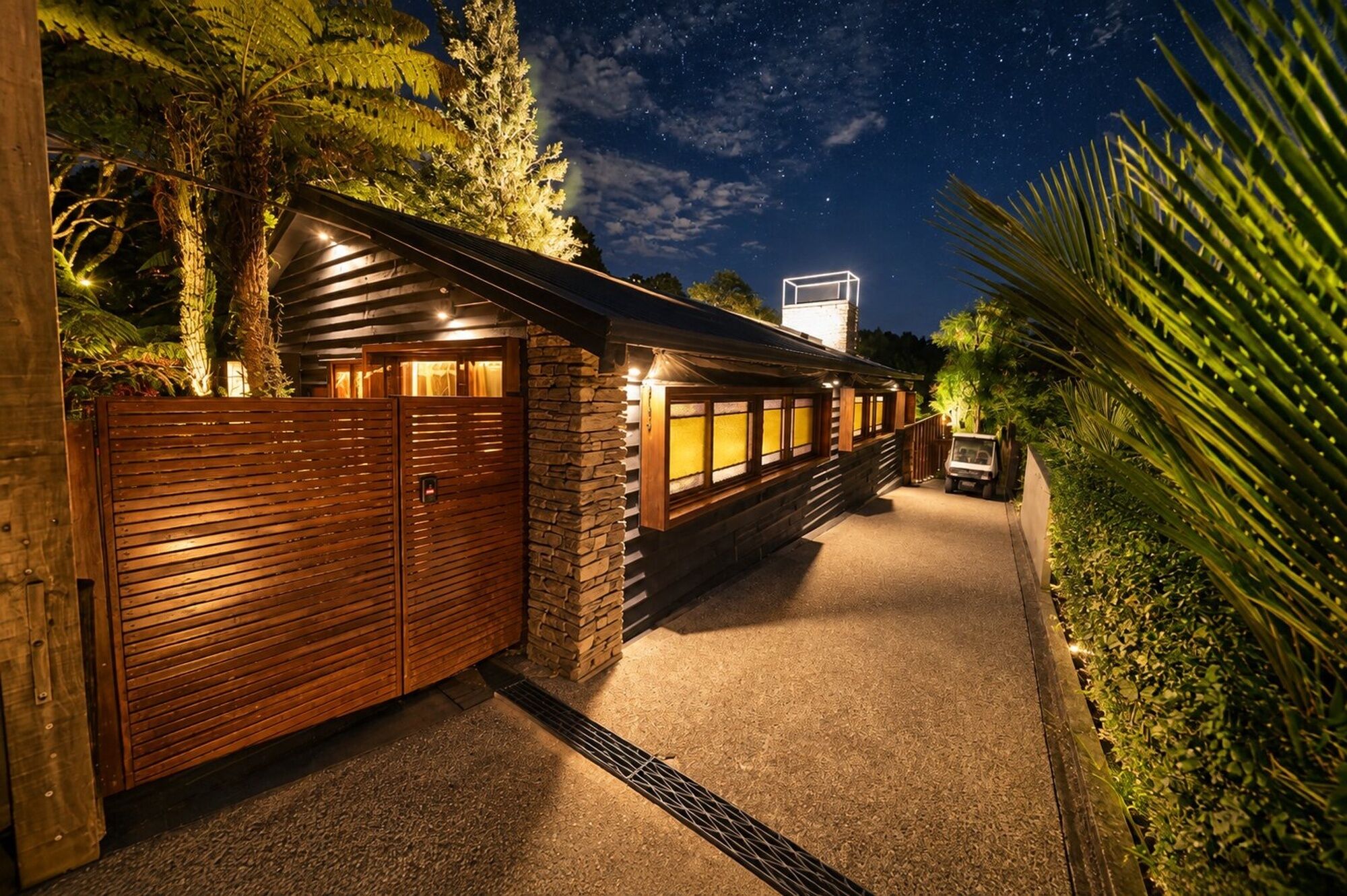 A well-lit wooden structure with a stone wall, a vehicle, and a clear night sky.