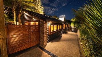 A well-lit wooden structure with a stone wall, a vehicle, and a clear night sky.