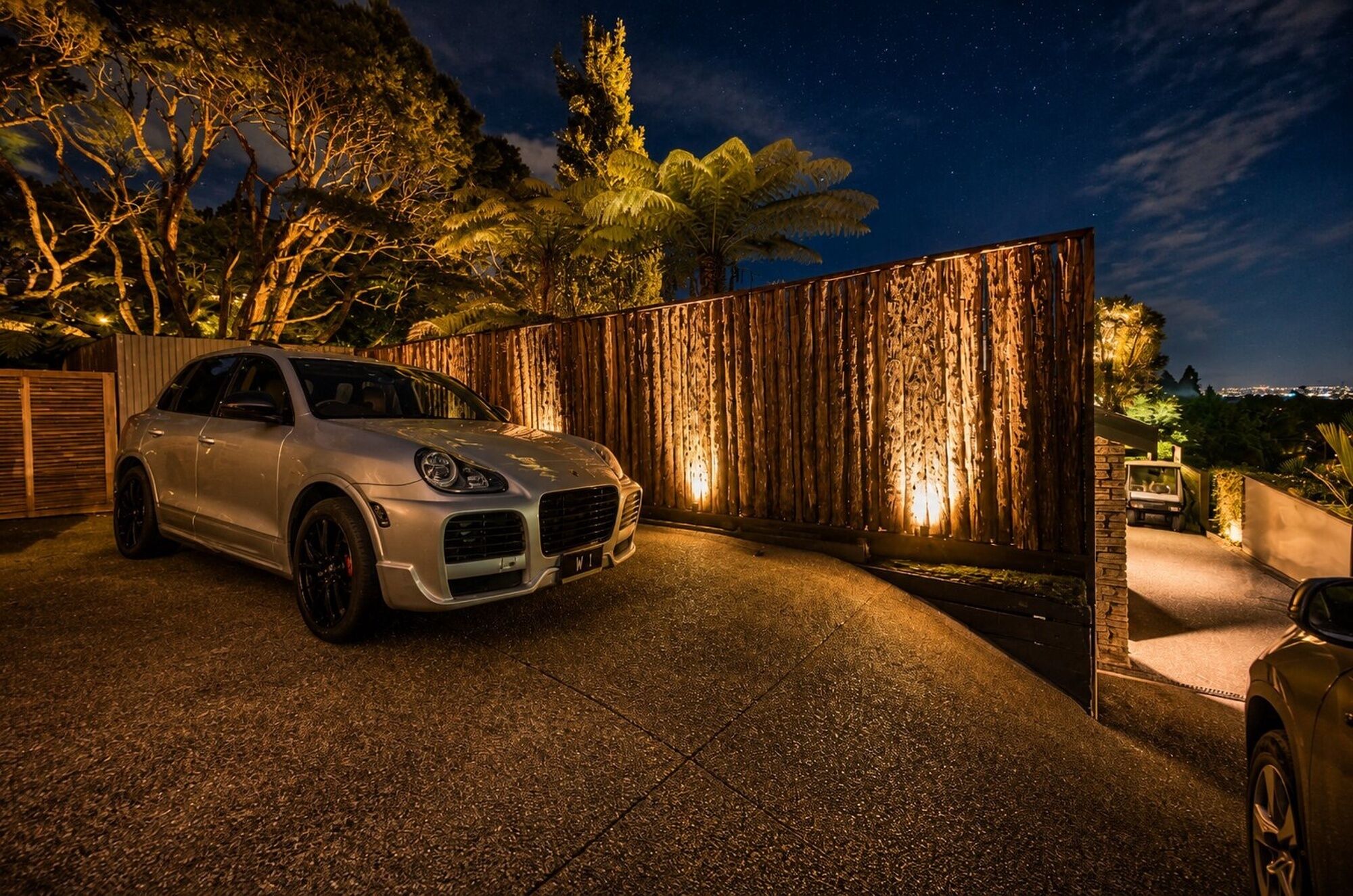 A white car parked in front of a wooden fence with a starry night sky in the background.