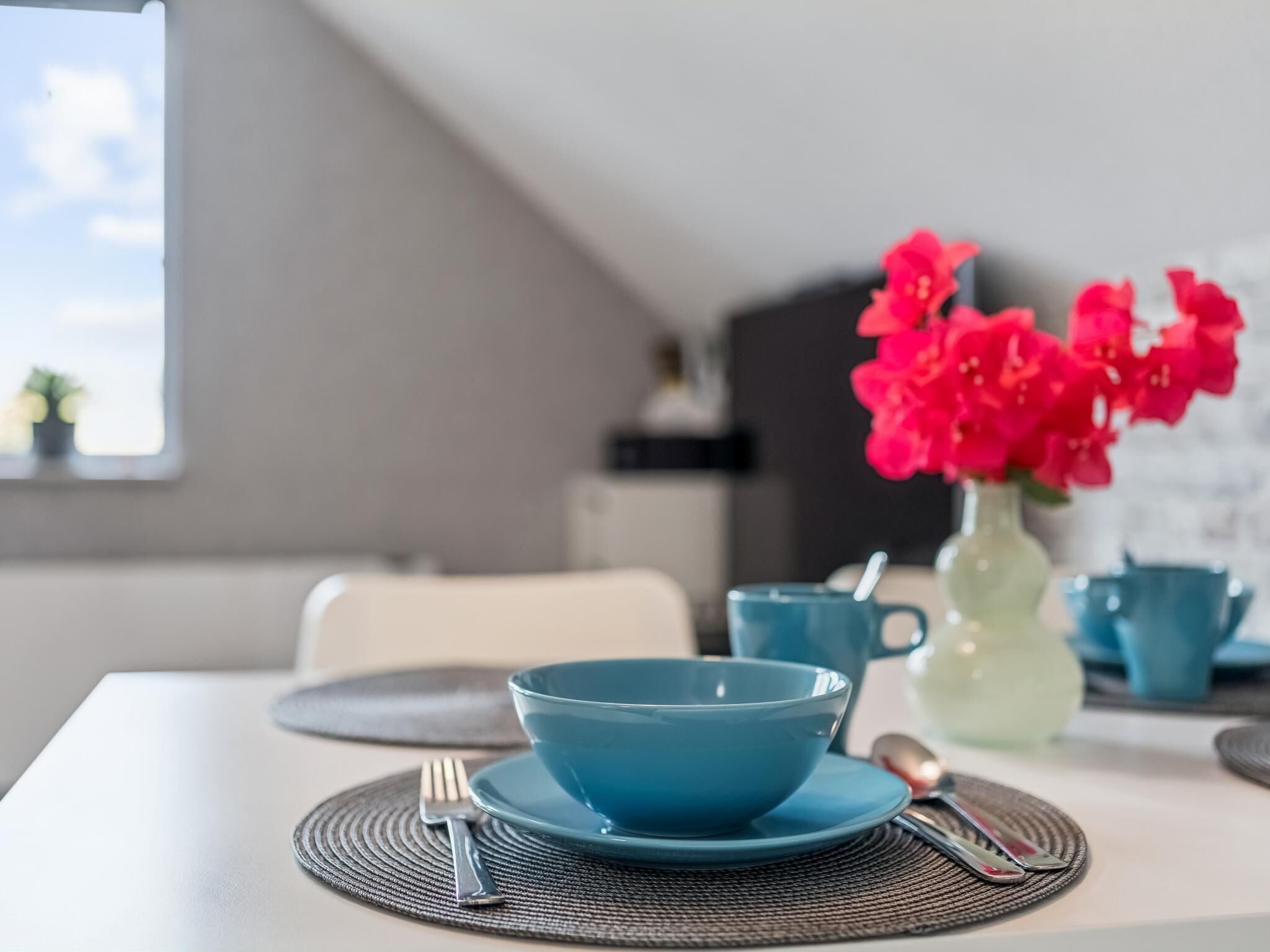 Une table à manger avec un bol bleu, une cuillère et une fourchette posés sur un set de table en fibres tressées.