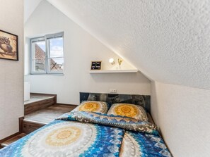 Ein Schlafzimmer mit einem Bett, einem Fenster, einem Regal mit Dekoration und einer Treppe.