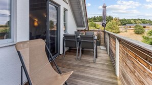 En balkong med ett bord och stolar, en flätstol och utsikt över omgivningen.