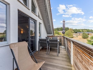 Ein Balkon mit Tisch und Stühlen, ein Korbstuhl und Blick auf die Umgebung.