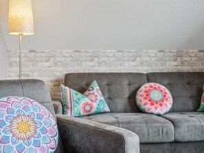 Ein graues Sofa mit bunten Kissen und einer Lampe in einem Raum mit Backsteinwand.