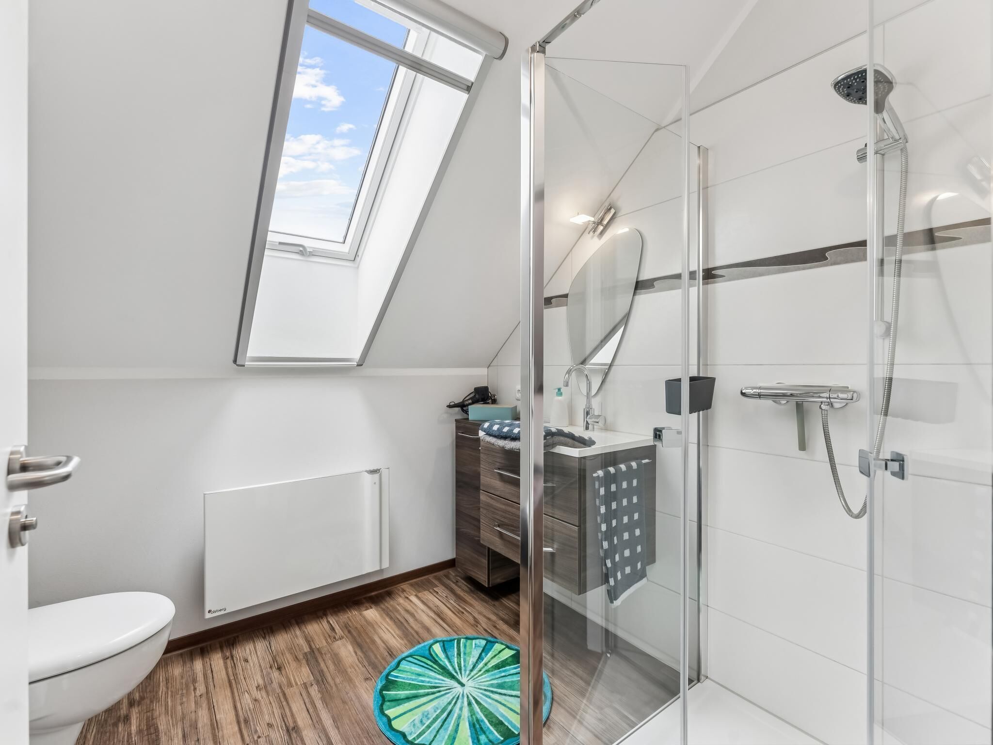 A modern bathroom with a skylight, a glass-enclosed shower, and a wooden floor.