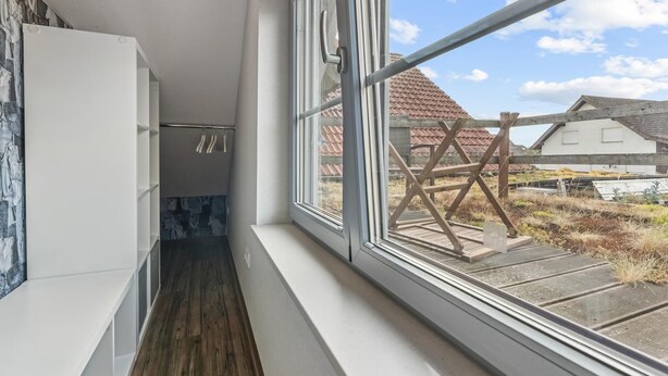 En smal hall med trägolv och ett stort fönster med utsikt över ett lantligt landskap.