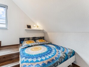 Quarto com cama, mesa de cabeceira, prateleira com um aviso e janela.