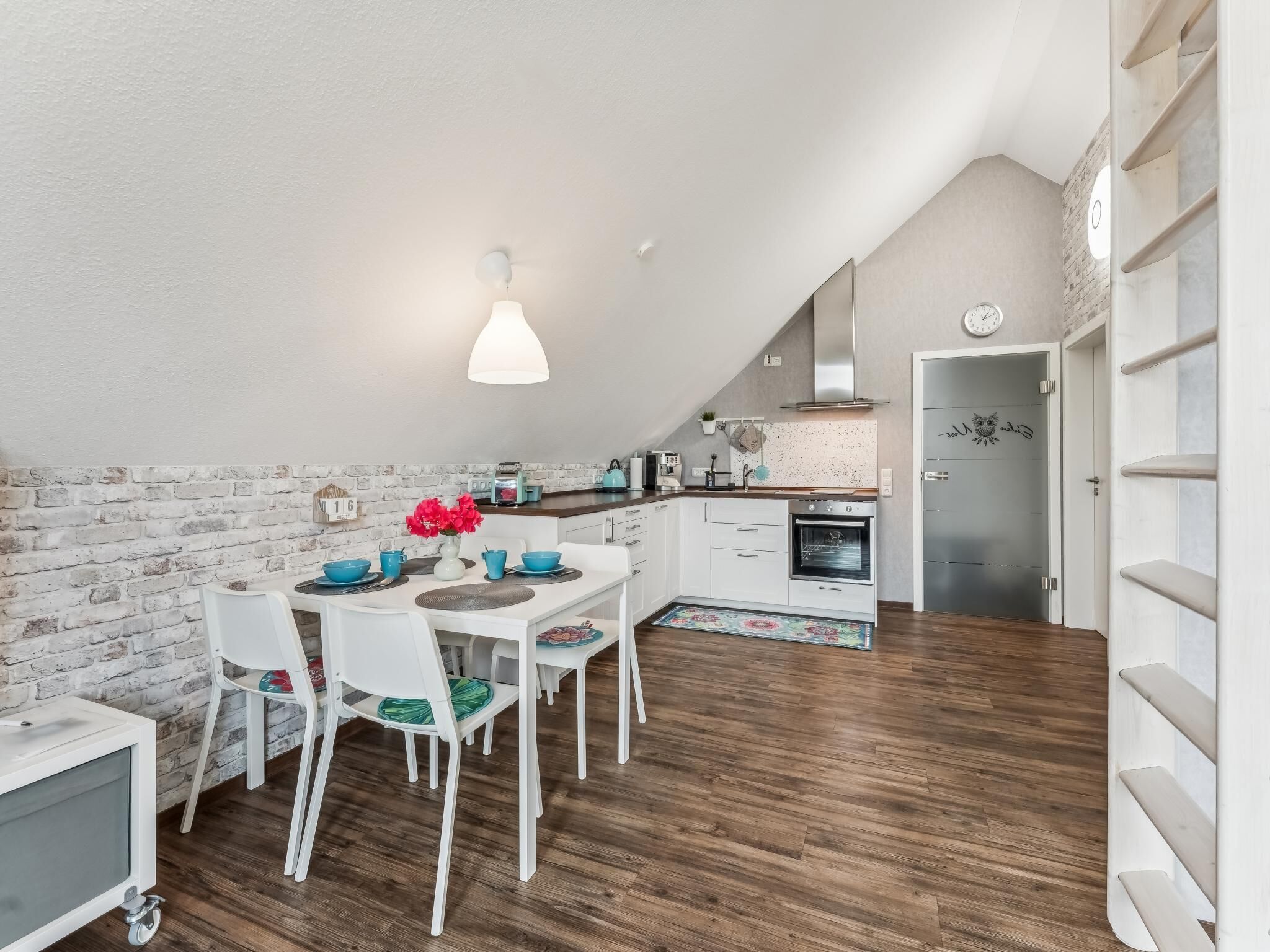 Een moderne keuken met witte kastjes, een houten vloer en een eethoek met witte stoelen en een tafel.