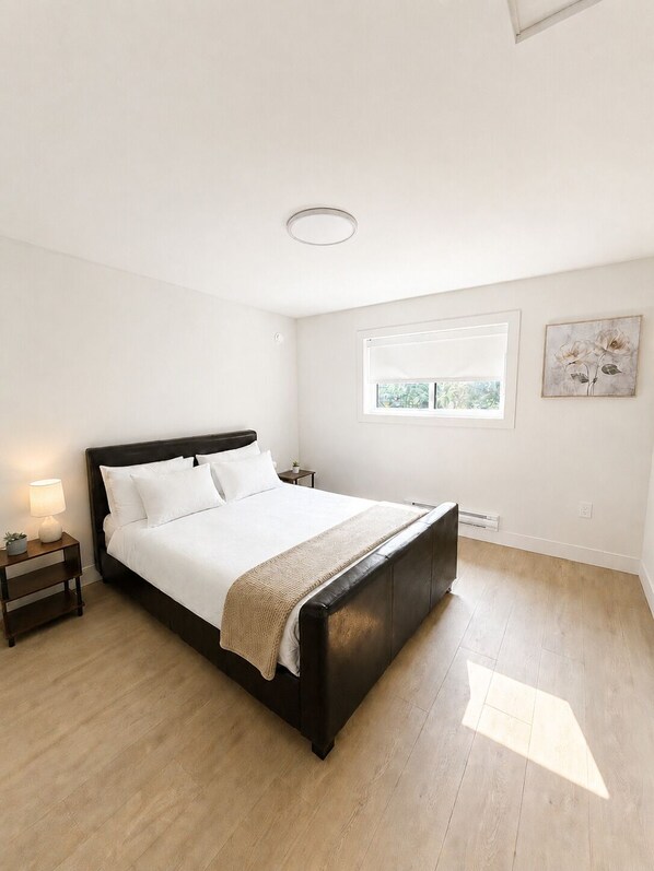 Een slaapkamer met een groot bed, een nachtkastje met een lamp, een raam met uitzicht en een aan de muur hangend kunstwerk.