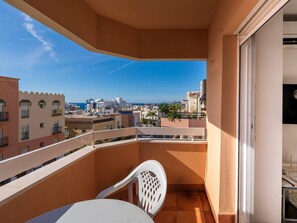 Ein Balkon mit weißem Stuhl und Tisch, der auf einen Stadtblick mit Gebäuden und blauem Himmel blickt.