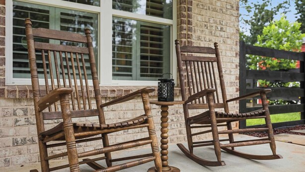 Two wooden rocking chairs with a small table between them, positioned in front of a brick house with large windows. - Big Ridge Hideaway Hot Tub (Talking Rock)