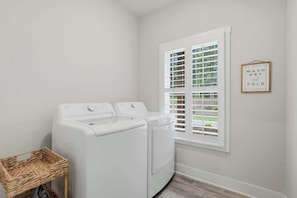A laundry room with two white front-loading washing machines, a wicker basket, and a window with white shutters. - Big Ridge Hideaway Hot Tub (Talking Rock)