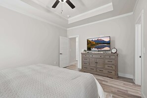 Ein Schlafzimmer mit einem Bett, einem Schminktisch, einem an der Wand befestigten Fernseher und einem Deckenventilator.