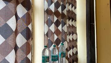 A hotel room with a wooden dresser, a mirror, and a patterned curtain. There are three water bottles on the dresser.