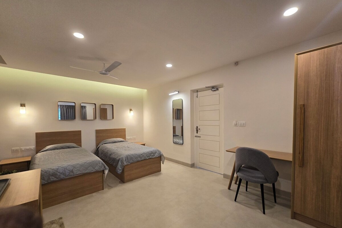A bedroom with two beds, a desk, a chair, a wardrobe, and a ceiling fan.
