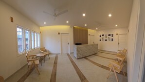 A reception area with a reception desk, seating area with chairs, and a ceiling fan. - Just Rooms (Chikkamagaluru)