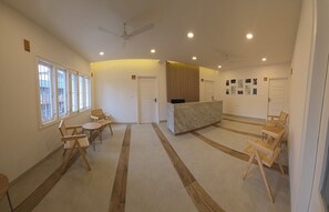 A reception area with a reception desk, seating area with chairs, and a ceiling fan. - Just Rooms (Chikkamagaluru)