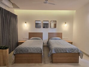 A bedroom with two beds, a ceiling fan, and wall-mounted mirrors. - Just Rooms (Chikkamagaluru)
