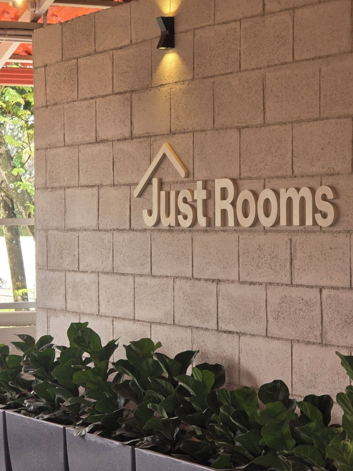 Una pared con un letrero que dice 'Just Rooms' y una jardinera con follaje verde.