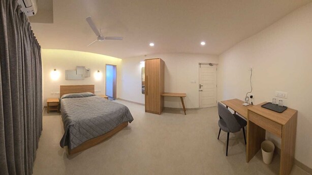 A hotel room with a bed, desk, chair, wardrobe, and a ceiling fan. - Just Rooms (Chikkamagaluru)