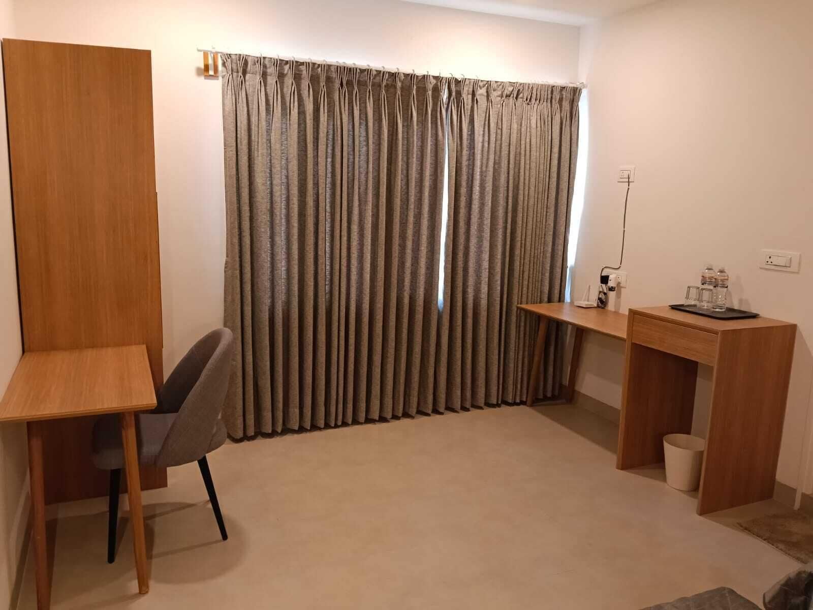 A room with a desk, chair, and a window with curtains.