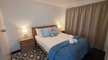 Een hotelkamer met een bed, nachtlampjes, een nachtkastje, een kamerbreed tapijt met een patroon en een raam met gordijnen.