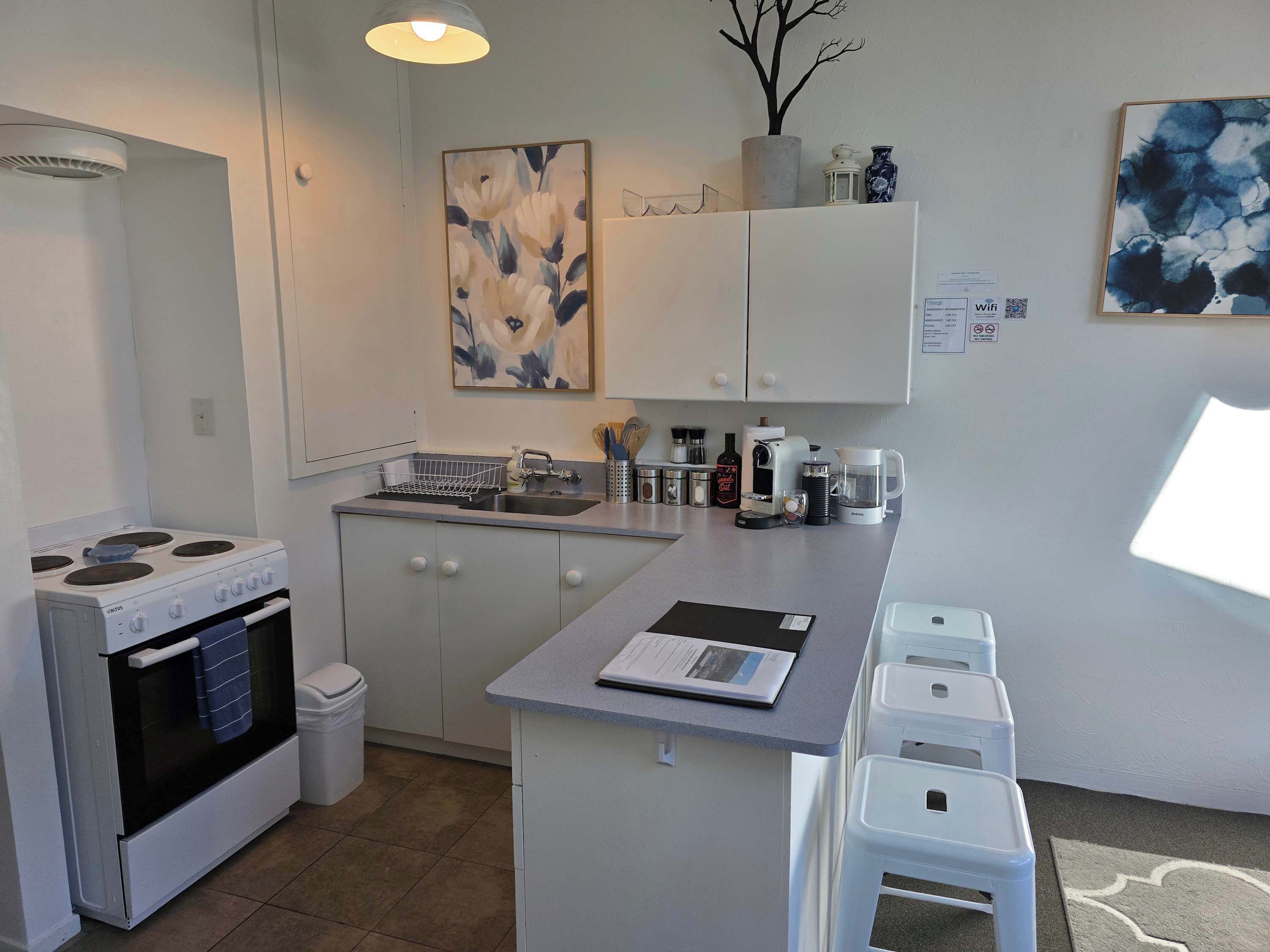 A compact kitchen with white cabinets, a stove, a sink, and a small island with stools.