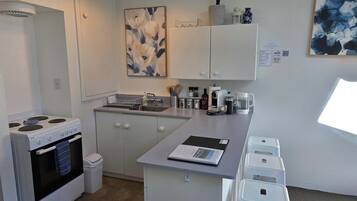 A compact kitchen with white cabinets, a stove, a sink, and a small island with stools.