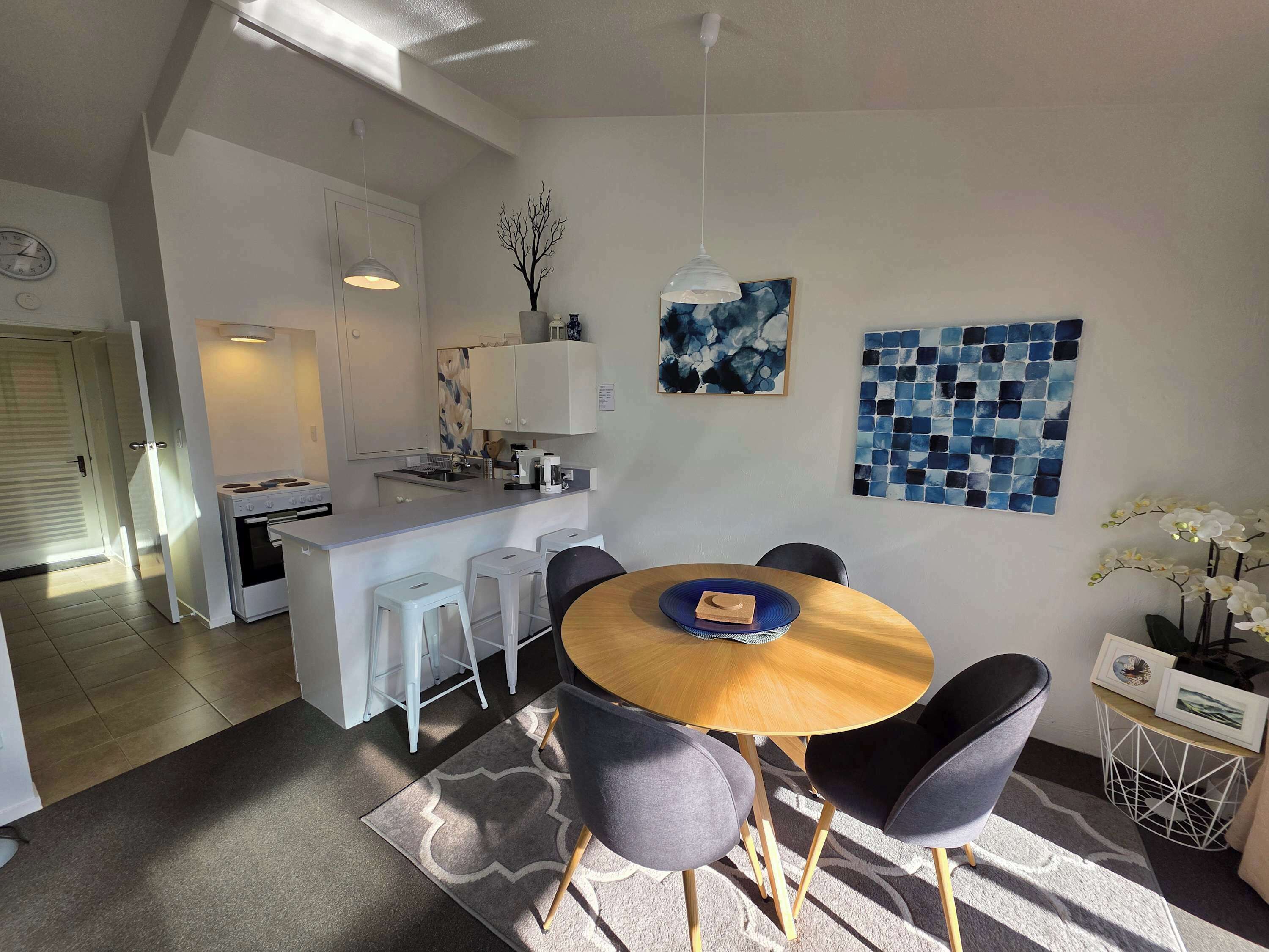 A modern kitchen with white cabinets, a dining area with a round wooden table and grey chairs, and a living space with a sofa and decorative items.