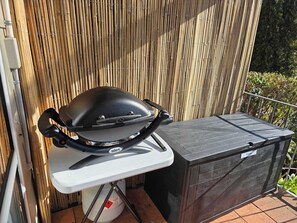Una parrilla portátil en un balcón con una valla de bambú al fondo.