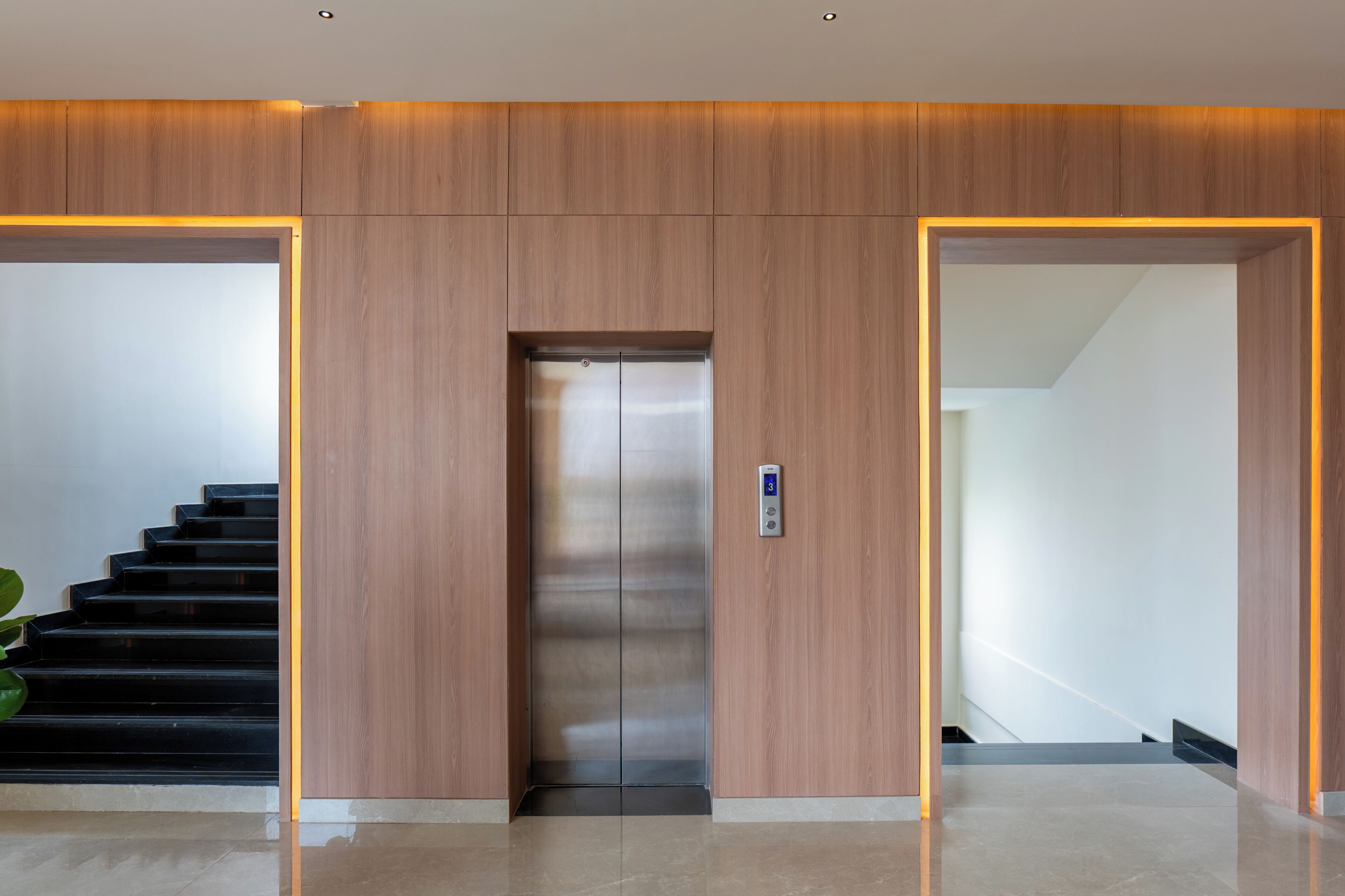 Un ascensor moderno con pantalla digital, flanqueado por paneles de madera e iluminación empotrada.