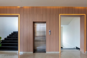 Un ascensor moderno con pantalla digital, flanqueado por paneles de madera e iluminación empotrada.
