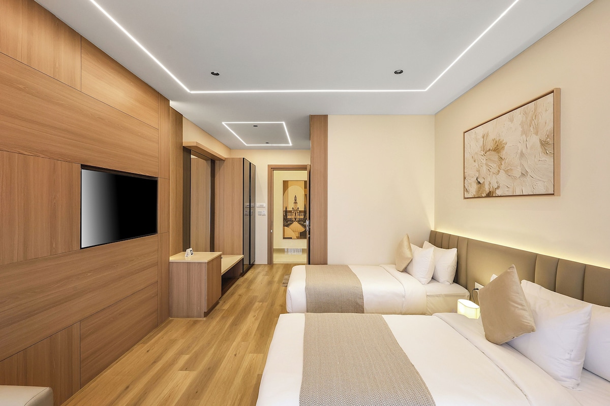 Ein Hotelzimmer mit Holzboden, einem Flachbildfernseher, einem Bett mit weißer Bettwäsche, einem Kopfteil mit integrierter Beleuchtung und einem Bild an der Wand.