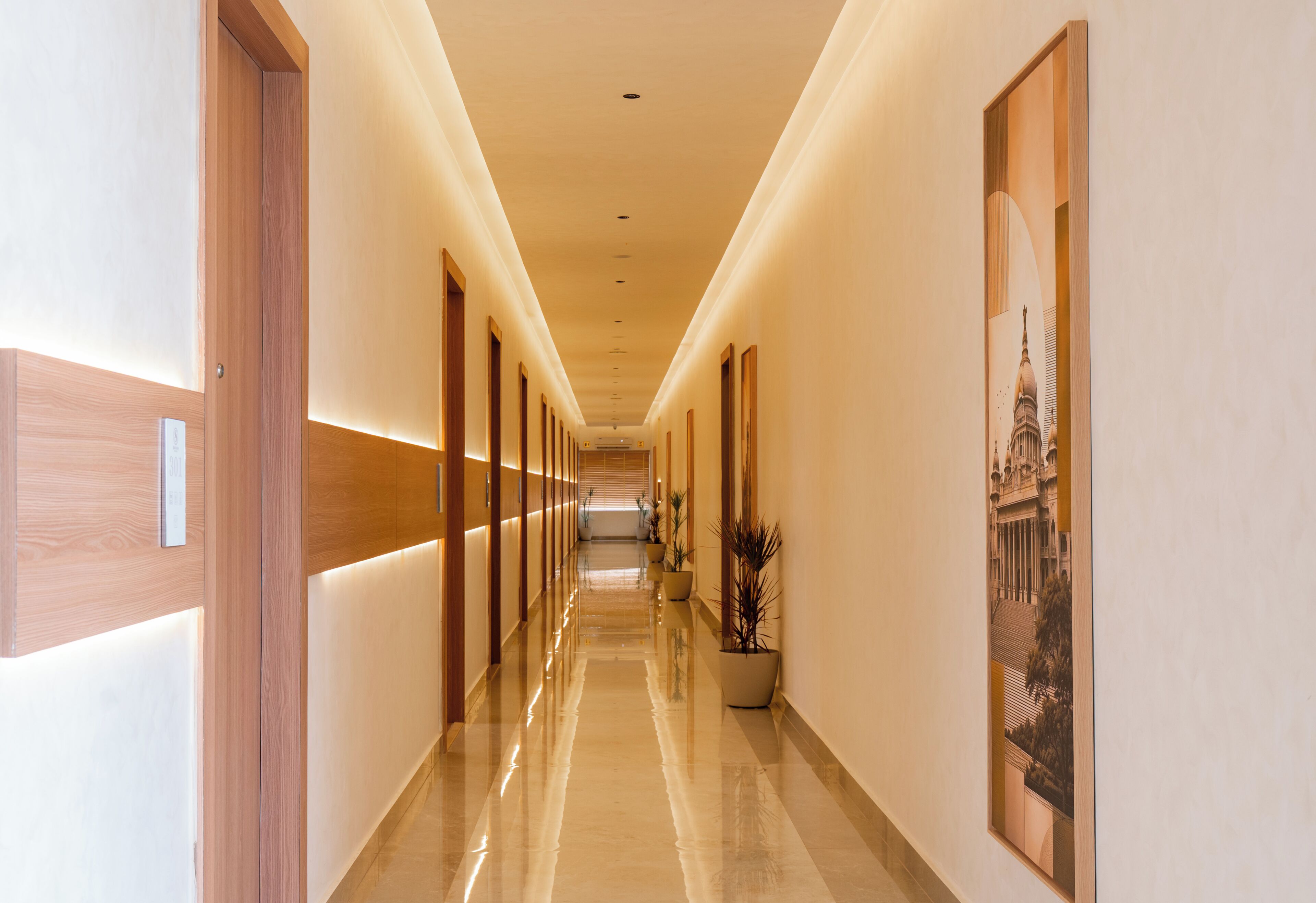 A hotel corridor with wooden doors, a polished floor, and framed artwork on the walls.