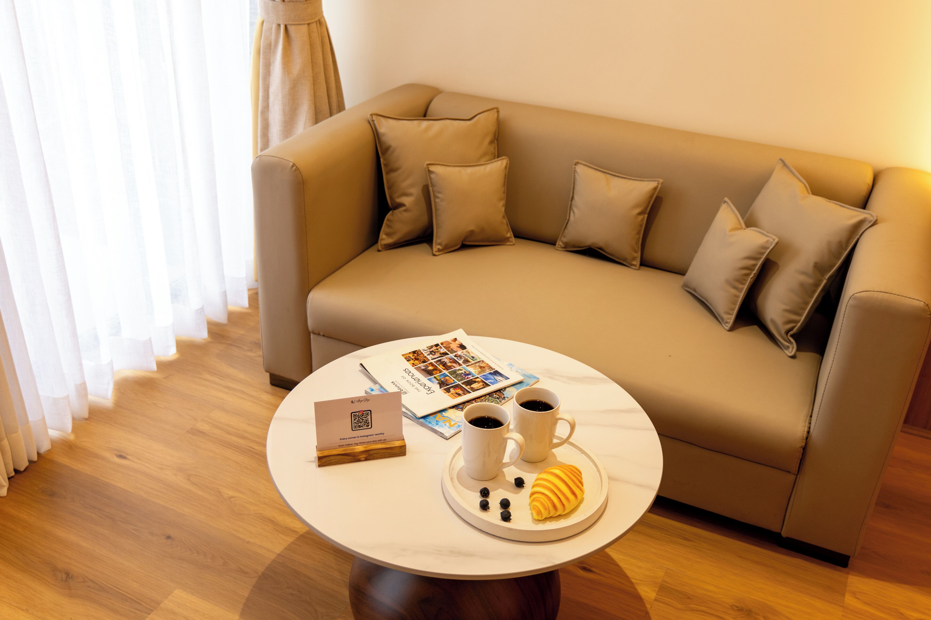 A cozy living area with a sofa, a coffee table with a tray of croissants and coffee cups, and a magazine.
