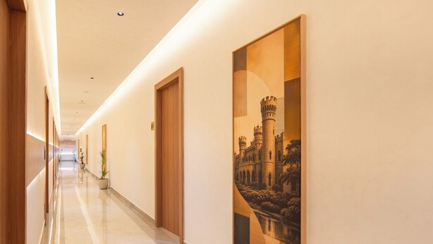 A hotel corridor with wooden doors, a polished floor, and a large framed picture on the wall. - ALAYA STAYS SAVIAN Suites (Chikkajala)