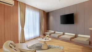 A modern living room with a flat-screen TV, leather sofas, a coffee table with decorative items, and a large window with curtains. - ALAYA STAYS SAVIAN Suites (Chikkajala)